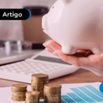 Pessoa segurando cofrinho de porquinho com moedas e calculadora sobre a mesa.