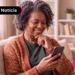 Senhora grisalha com a mão no queixo sorrindo olhando para o celular.