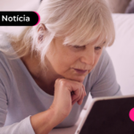Idosa deitada mexendo no tablet.