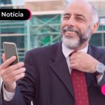 Homem de terno olhando para celular com expressão feliz.