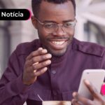 Homem em trabalho olhando para celular com expressão feliz.