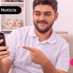 Jovem sorrindo enquanto usa celular para ler notícia sobre o novo desenrola brasil.
