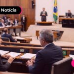 Pessoas em câmara de deputados olhando pessoa falando em microfone.