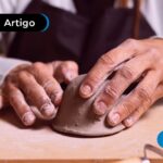 Mãos de uma idosa sentada na mesa fazendo artesanato de modelagem.