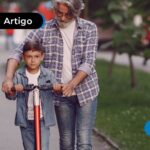 Avô ajudando seu neto a andar de patinete em uma praça.