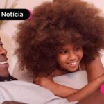 Pai e filha deitados na cama olhando para o celular.