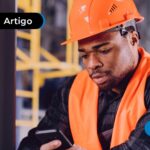 Trabalhador com uniforme e EPIs de segurança utilizando celular para ler artigo sobre uso do FGTS como garantia no Consignado CLT.