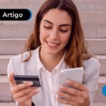 Mulher sorrindo e sentada em escada segurando um cartão e celular.