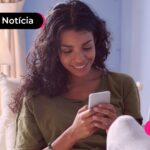 Mulher sorrindo ao acessar o celular.
