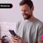 Homem de camisa cinza segurando um celular.
