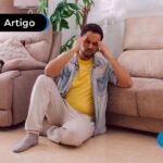 Homem sentado no chão da sala demonstrando uma feição de mal estar.