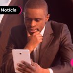 Homem de traje social segurando celular expressando dúvidas.