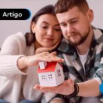 Casal sentados no sofá segurando uma casa em miniatura.