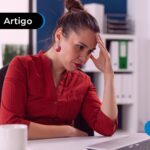 Mulher sentada em uma sala olhando para o notebook com feição de preocupação.