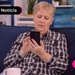 Idosa sentada em um sofá fazendo o uso de celular.