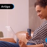 Mulher sentada no sofá segurando um iPad e um cartão de crédito.