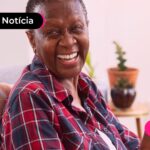 Idosa sorrindo para a foto com um celular nas mãos.