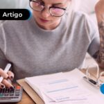 Mulher usando uma calculadora e uma pasta em cima da mesa exibindo documento.