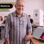 Idoso rindo em uma seção eleitoral ao lado de uma urna.