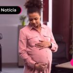 Mulher gestante de vestido rosa segurando a barriga.