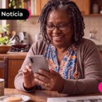 Idosa sentada na cozinha olhando para o celular.