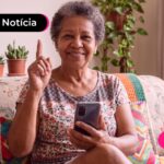 Idosa sentada no sofá da sala sorrindo para a foto.