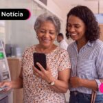 Idosa e uma jovens sorrindo para a foto e utilizando o caixa eletronico.
