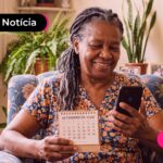 Idosa sentada na cadeira da sala segurando um calendário.