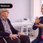 Profissional de interprete falando com um idoso de cadeira de rodas.