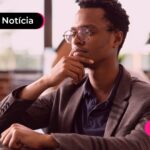 Jovem de roupa social com a mão apoiada no queixo pensativo.