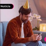 Homem sentado olhando para o celular e usando um chapéu de festa.