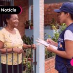 Uma agente da saúde conversando com uma idosa em frente sua casa.