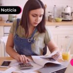 Mulher olhando documentos enquanto utiliza calculadora e notebook.