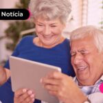 Casal de idosos rindo enquanto olham para tablet juntos.
