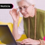 Idosa sentada no sofá enquanto utiliza notebook.