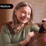 Idosa sentada no sofá olhando para o celular.