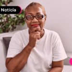Idosa aposentada sorrindo olhando para camera com pose pensativa.